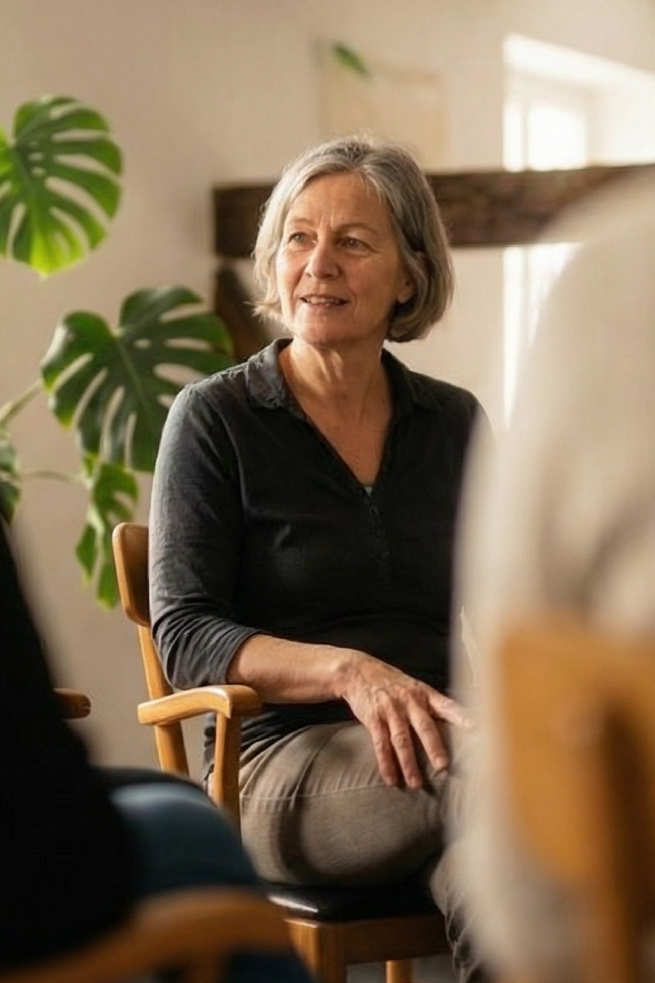 Eine lächelnde Frau sitzt in einem Stuhl und spricht in einer Gesprächsrunde, umgeben von Pflanzen.