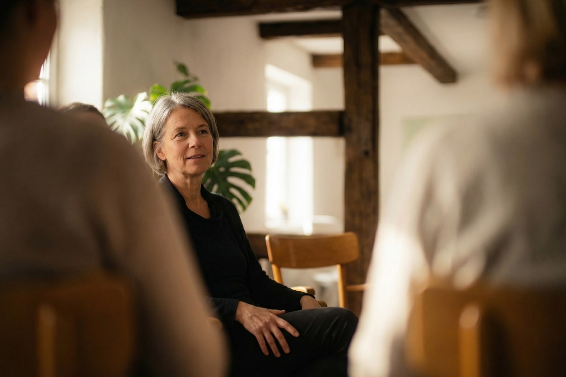 Eine Frau sitzt in einem Gesprächskreis und hört aufmerksam zu, umgeben von anderen Personen und Pflanzen.