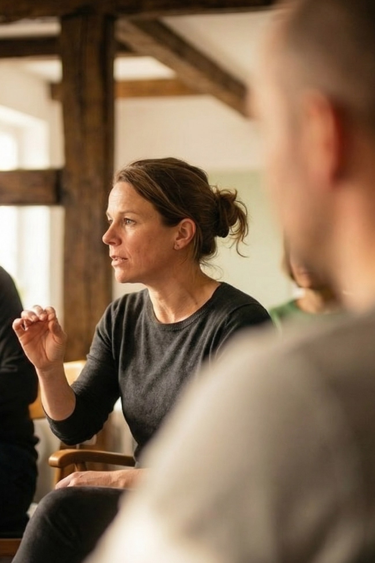 Eine Frau in einem Gespräch, die mit der Hand gestikuliert, während andere Teilnehmer im Hintergrund sitzen.