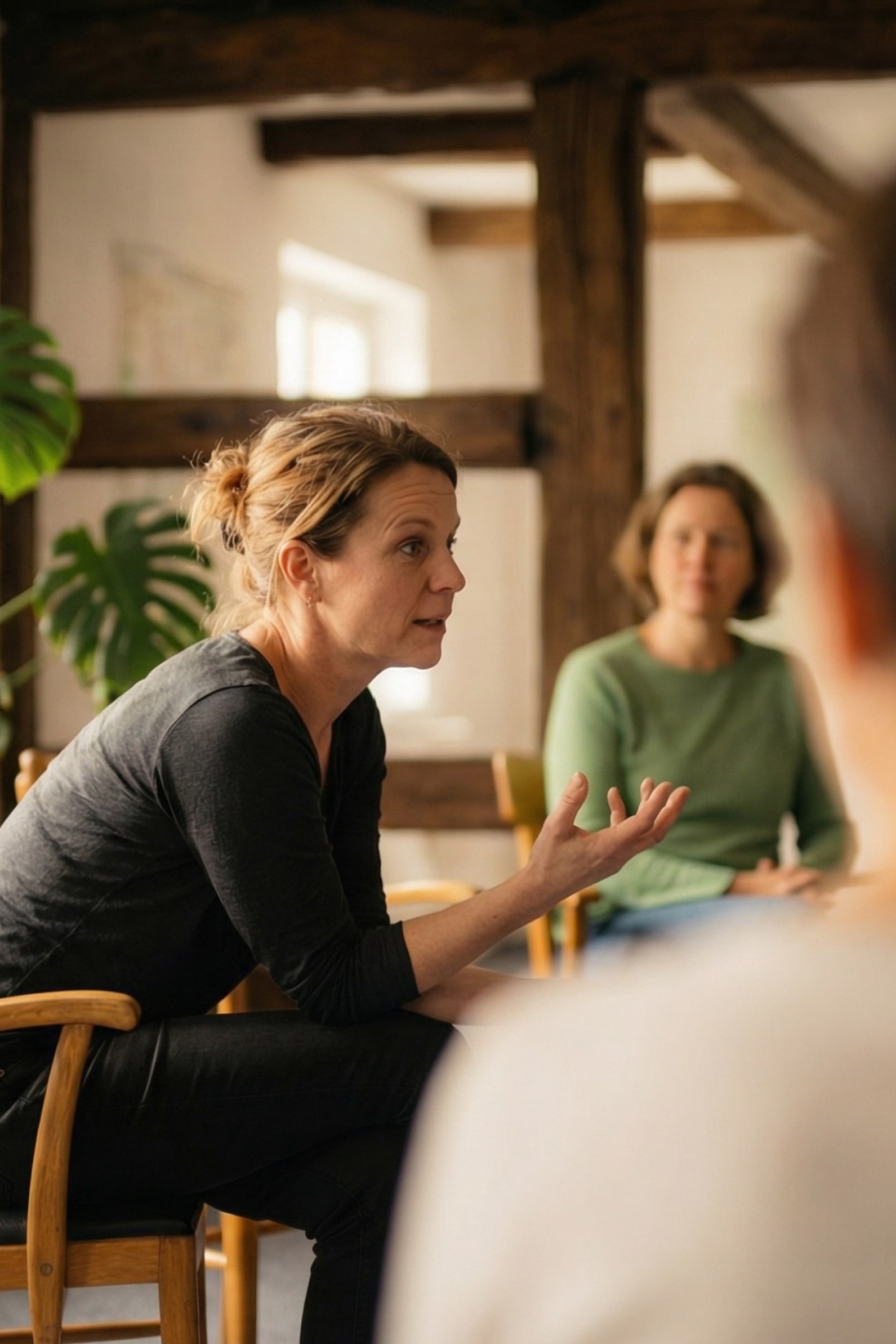 Eine Frau spricht in einer Gruppe, während eine andere Person im Hintergrund zuhört. Gemütliche Atmosphäre.