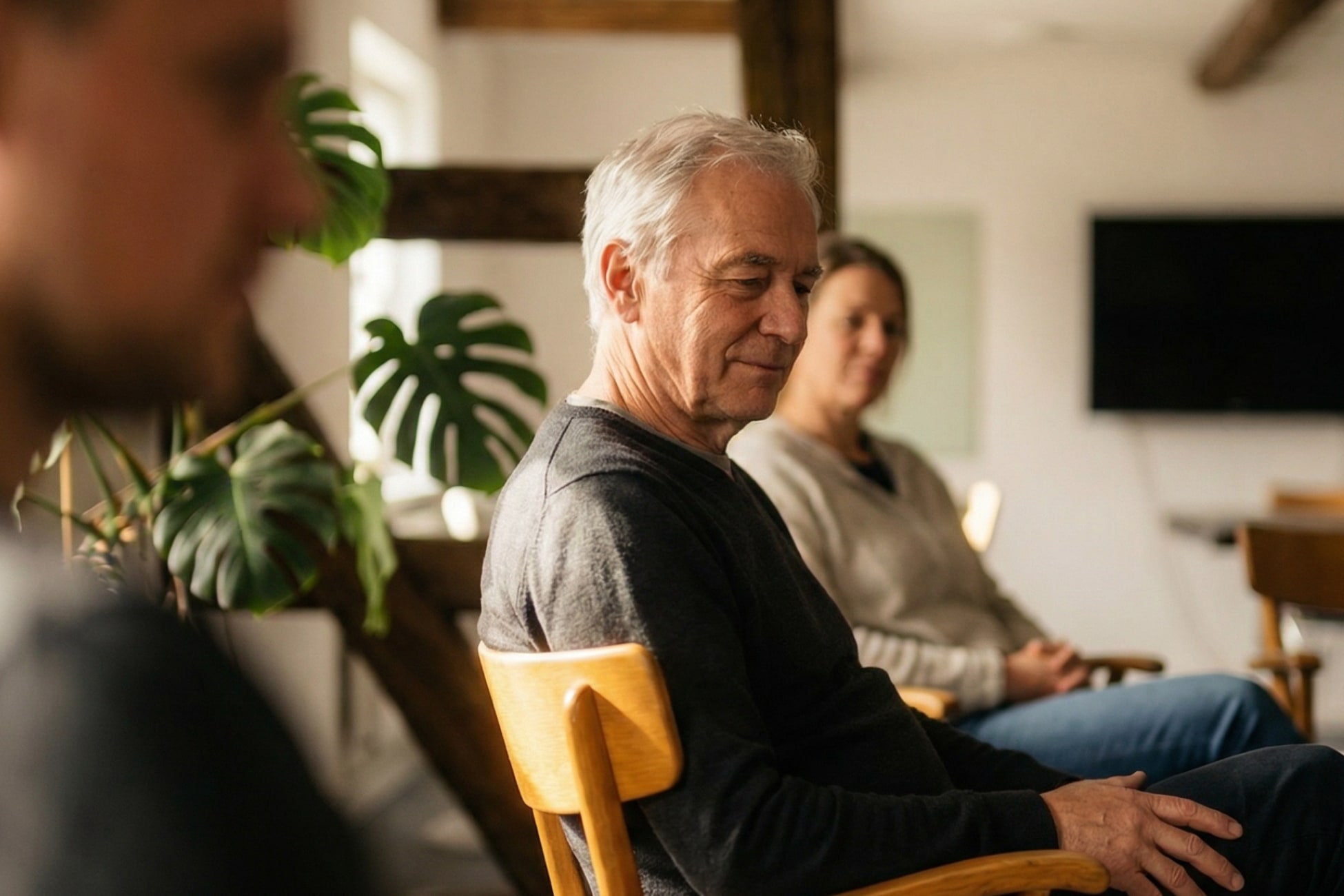 Drei Personen sitzen in einem Raum, eine Pflanze im Hintergrund, entspannte Atmosphäre.