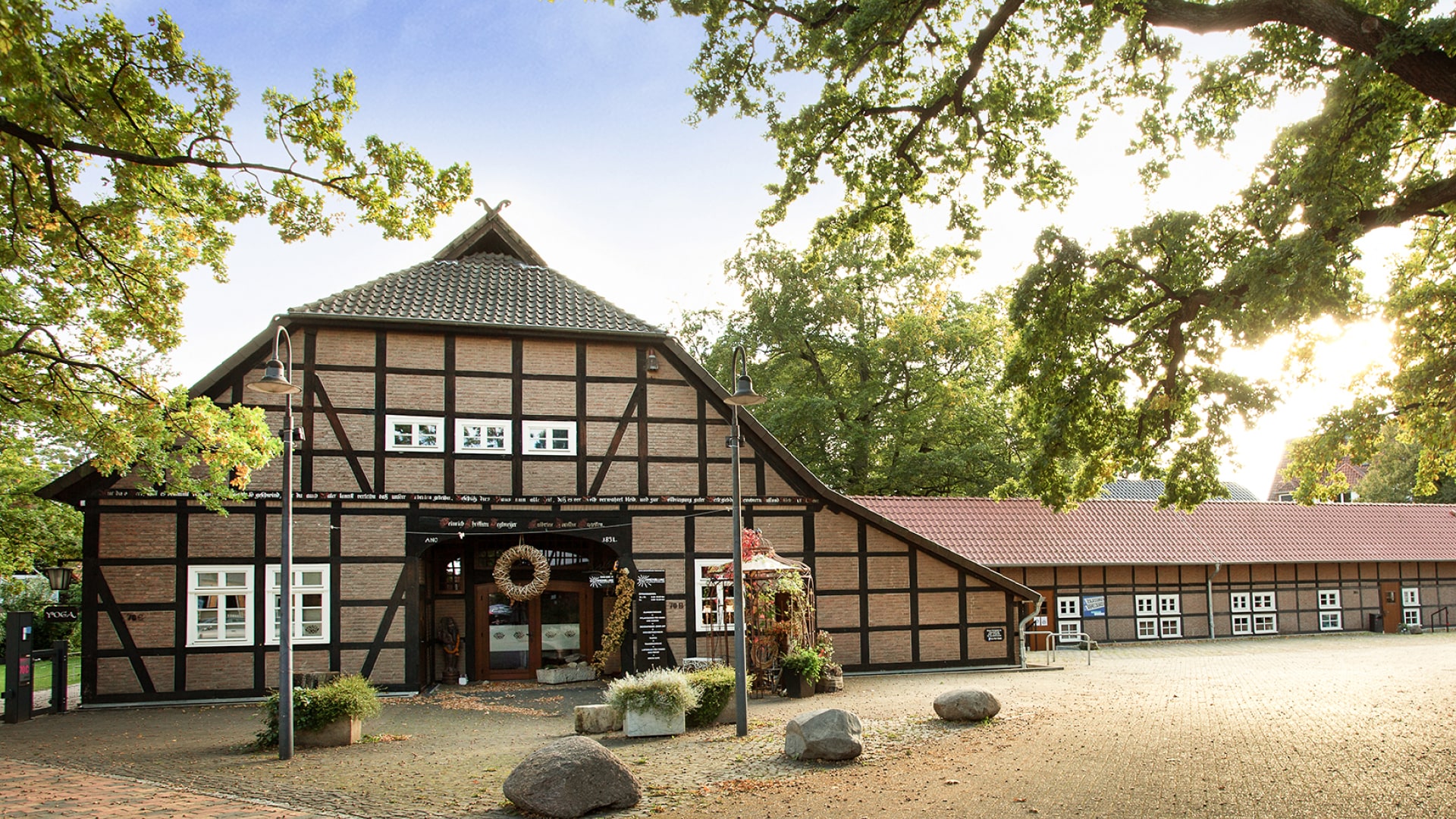 Historisches Fachwerkhaus umgeben von Bäumen, mit einem gepflasterten Vorplatz und einer einladenden Eingangstür.