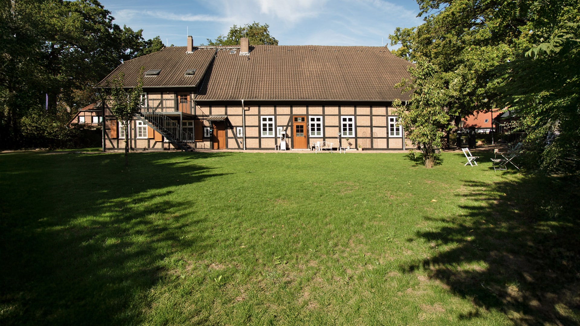 Ein historisches Gebäude mit Garten, umgeben von Bäumen und einer Terrasse im Freien.
