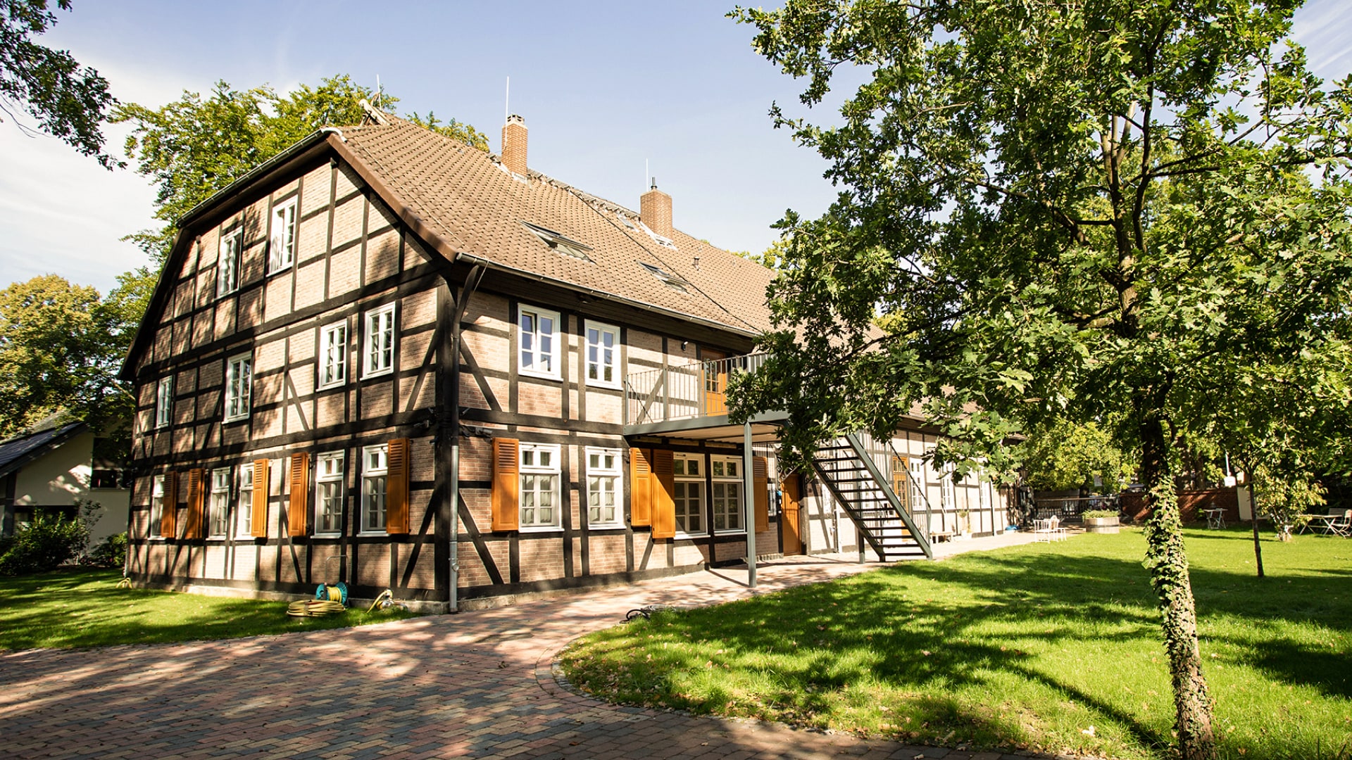 Historisches Fachwerkhaus mit Garten und Terrasse, umgeben von Bäumen und einem gepflasterten Weg.