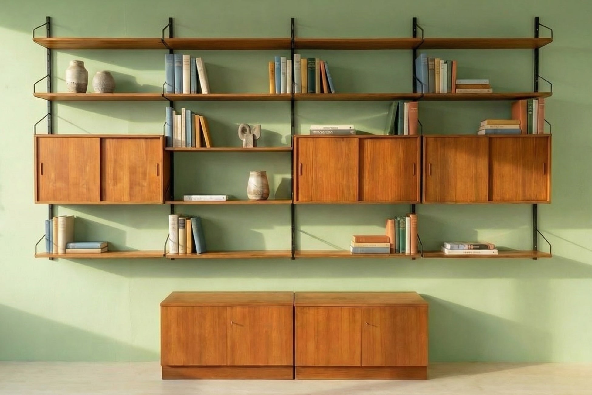 Regal mit Holzregalen, Büchern und dekorativen Objekten vor einer grünen Wand.